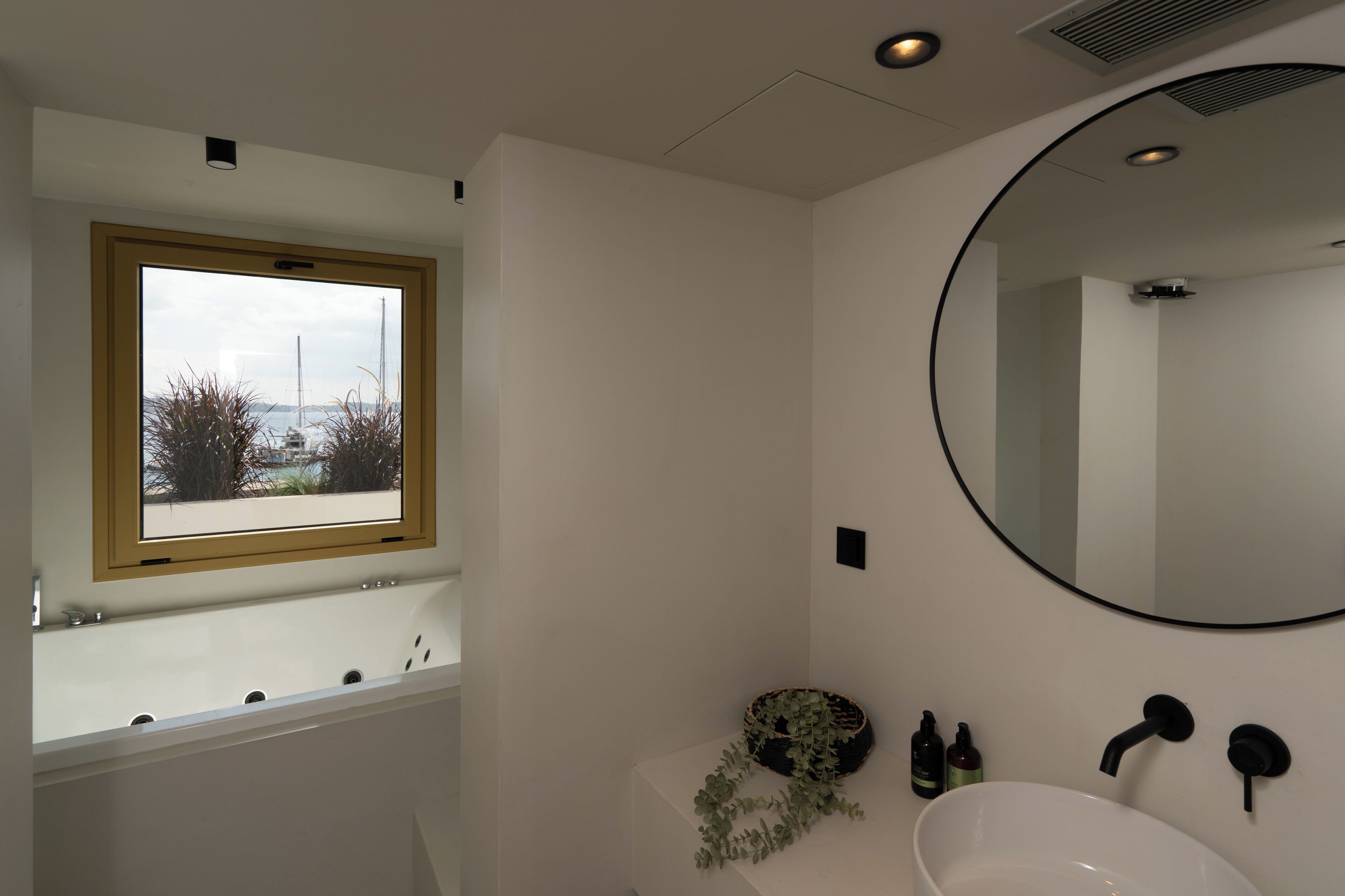 A modern bathroom with a bathtub, a sink, a mirror, and a window with a view of the outside.