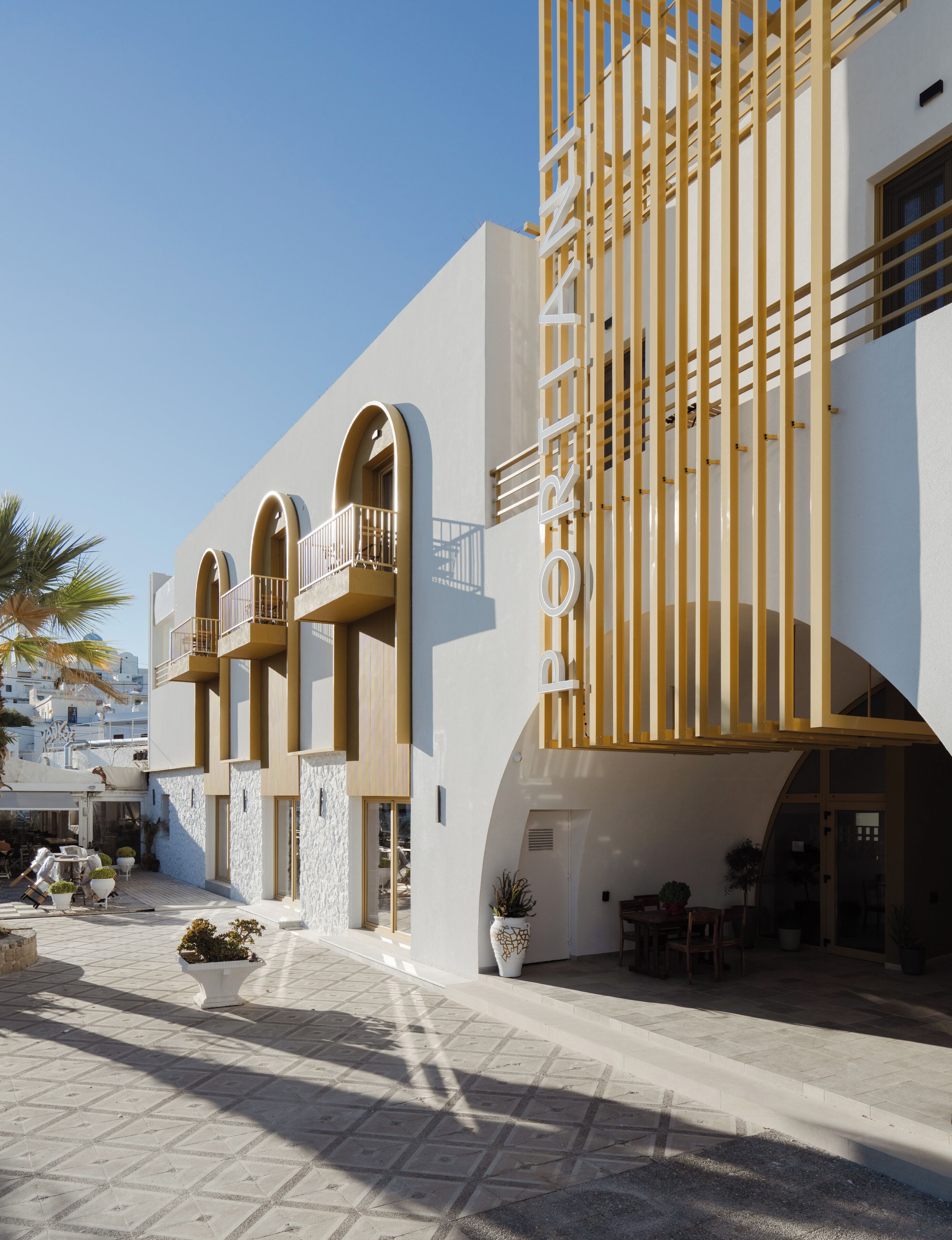 A modern building with a prominent 'ORT' sign, arched balconies, and a tiled courtyard with outdoor furniture.