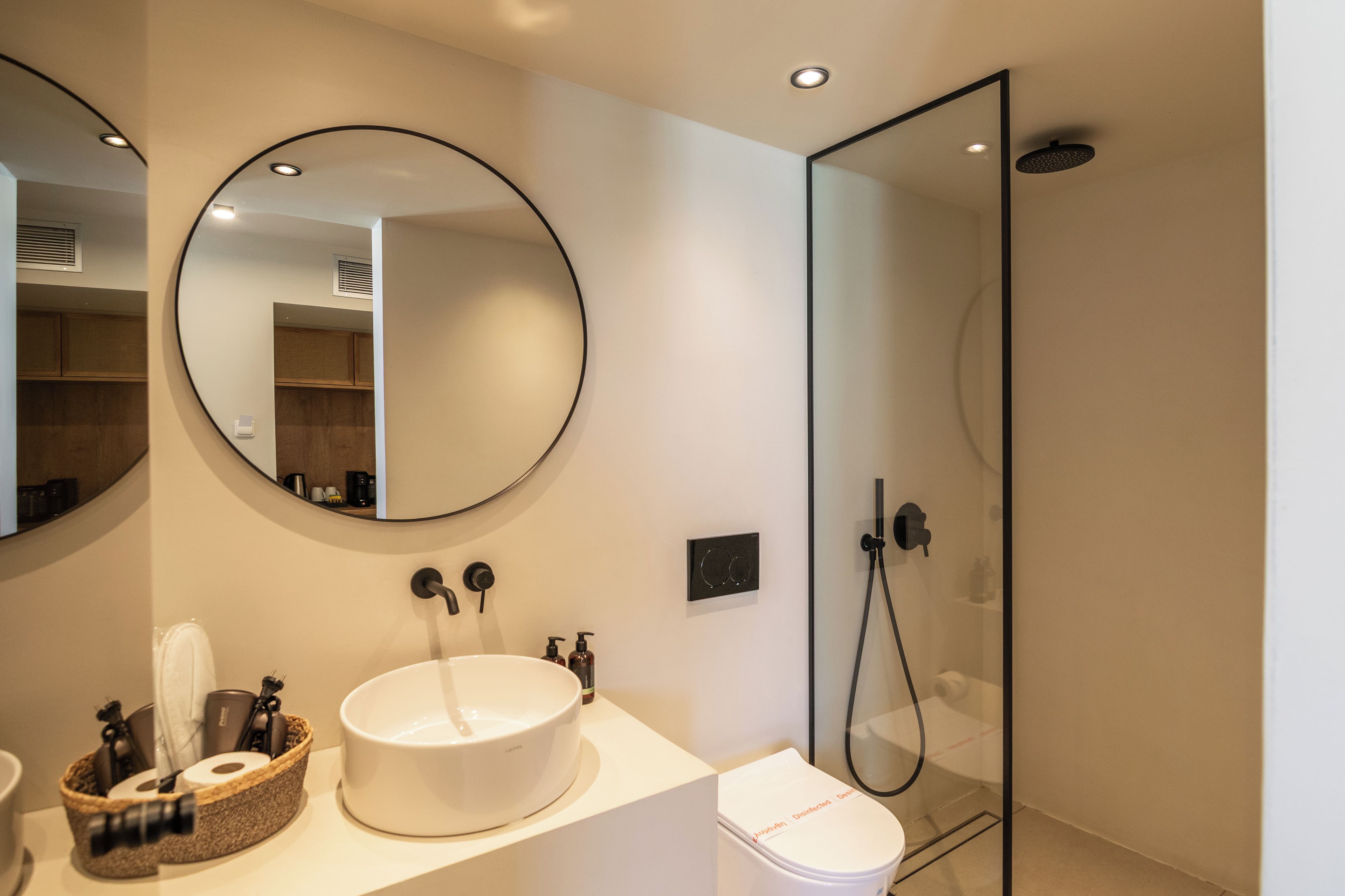 Ein modernes Badezimmer mit rundem Spiegel, weißem Waschbecken und einer Duschkabine aus Glas.