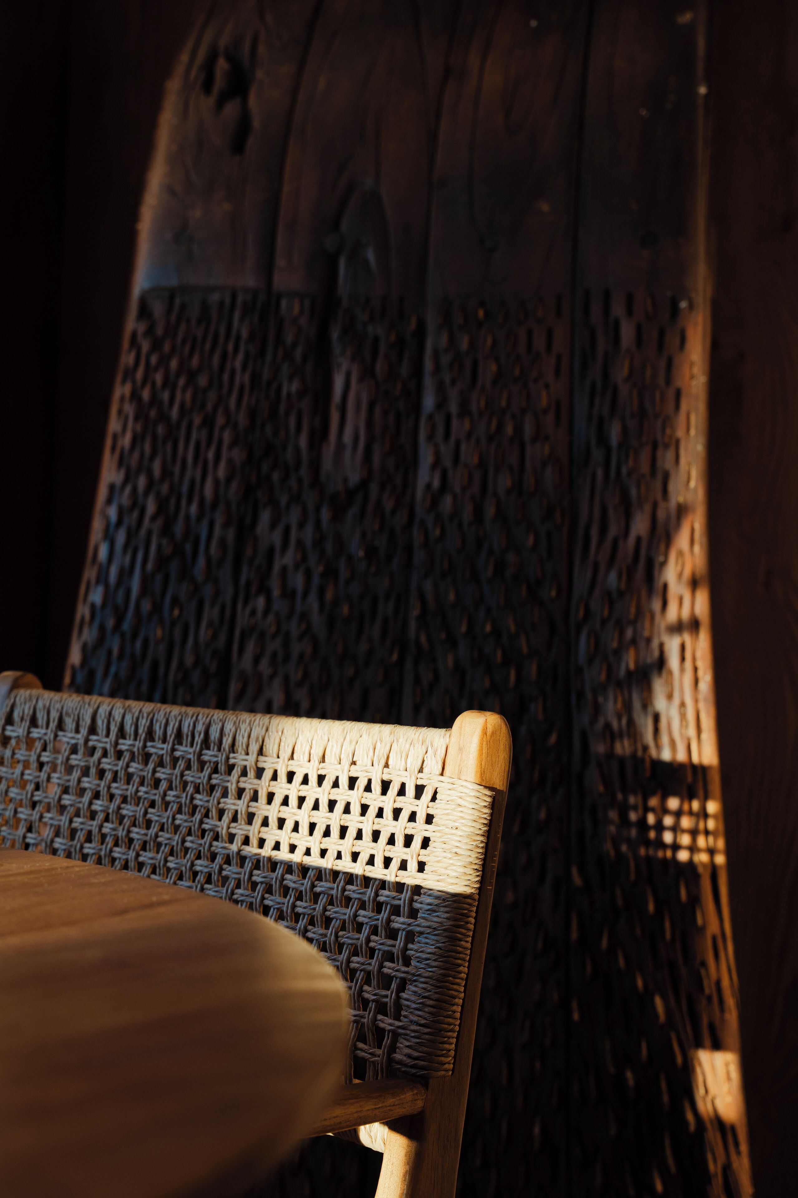Une chaise en osier, avec une assise et un dossier en fibres tressées, placée devant un mur en bois présentant un motif texturé.