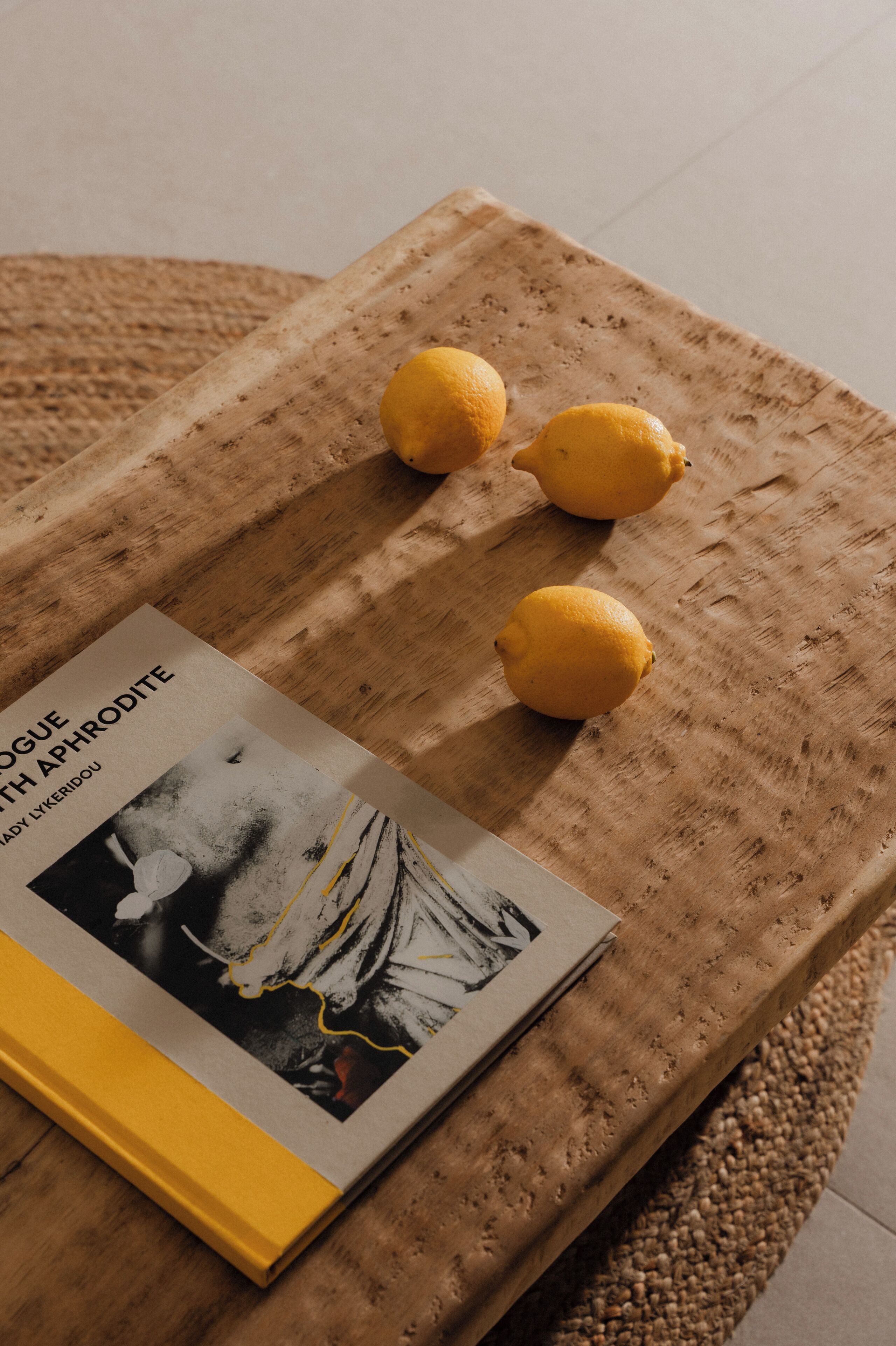 Un livre intitulé « Dogue avec Aphrodite » est posé sur une surface en bois, accompagné de trois citrons.