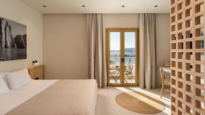 Une chambre avec un lit, une vue sur la mer par une porte vitrée, une tête de lit en bois et un tableau accroché au mur.