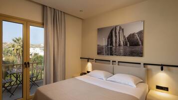 A hotel room with a bed, a nightstand, a wall-mounted lamp, a window with curtains, and a balcony with a table and chairs.