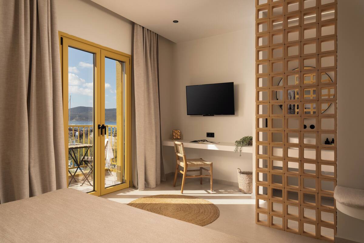 Et soveværelse med seng, skrivebord, stol, fjernsyn og en balkon med udsigt.