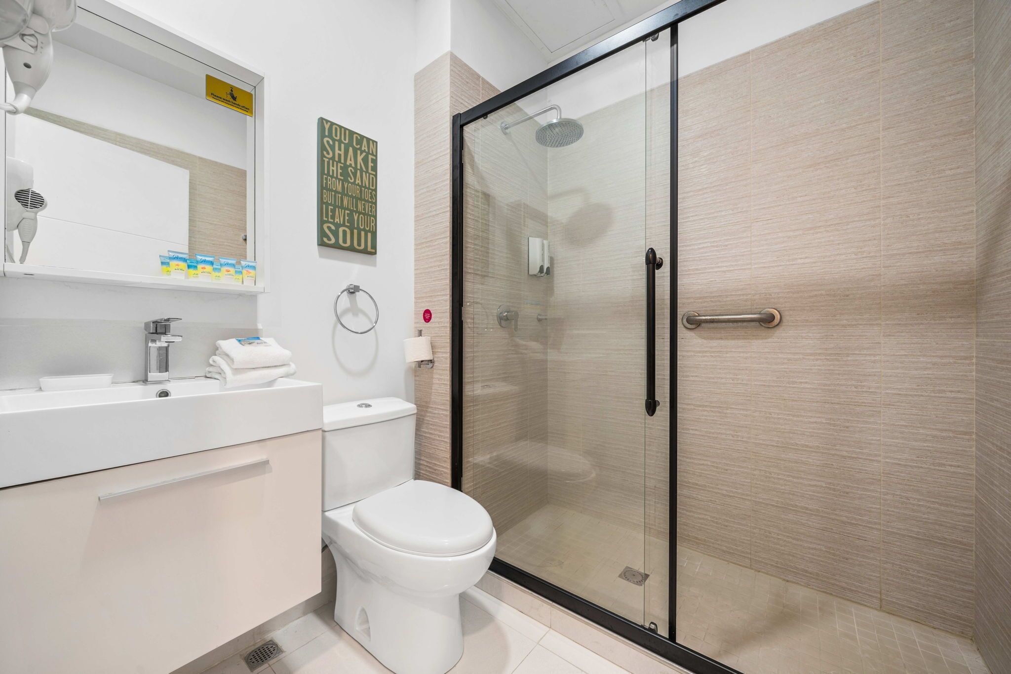 A modern bathroom with a glass-enclosed shower, a white toilet, and a vanity with a mirror and towel rack.