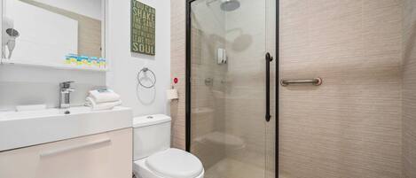 A modern bathroom with a glass-enclosed shower, a white toilet, and a vanity with a mirror and towel rack.