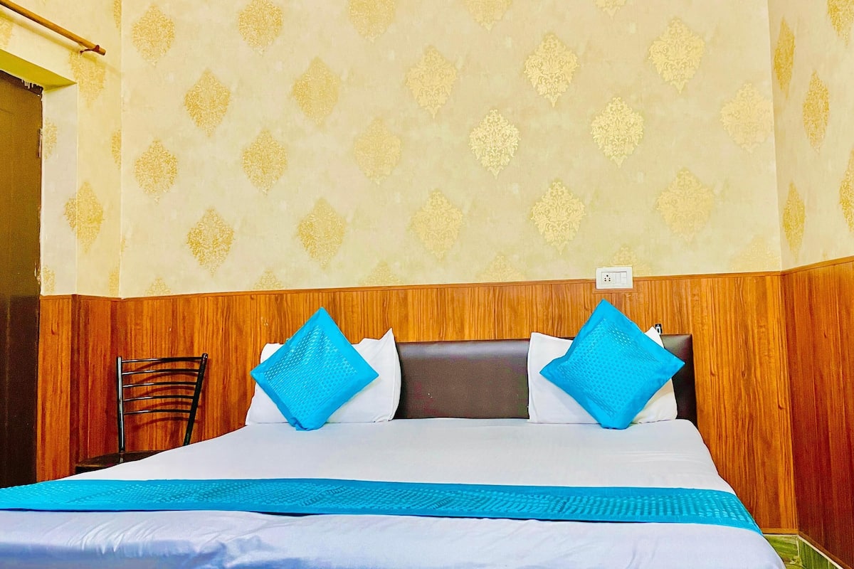 Hotellihuone, jossa on puinen sängynpääty, valkoisilla ja sinisillä tekstiileillä varustettu sänky sekä kuviollinen tapetti.
