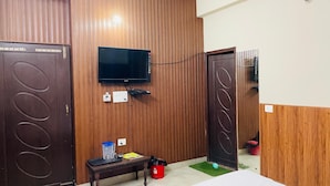 Une chambre d’hôtel avec des lambris en bois, un téléviseur à écran plat fixé au mur, une petite table avec un plateau, une poubelle rouge et une porte ornée d’un motif circulaire.