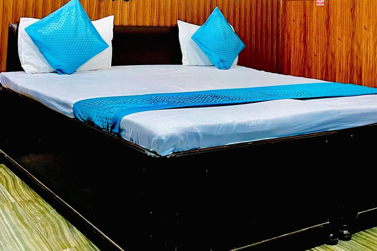Hotellihuone, jossa on puupaneloitu seinä, sinisellä tekstiilillä varustettu sänky ja kaksi kehystettyä kuvaa seinällä.