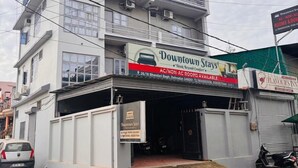 Un immeuble à plusieurs étages, sur lequel on peut lire une enseigne indiquant « Downtown Stay », et qui propose des chambres avec ou sans climatisation.