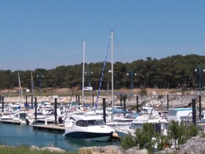 Un port de plaisance où sont amarrés des bateaux, entouré d’un paysage rocheux et d’une colline boisée.
