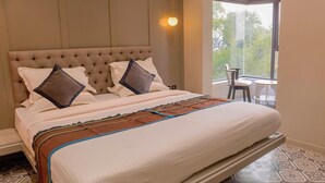 A neatly made bed with a tufted headboard, a patterned bedspread, and a view of the outdoors through a window. - The 12th Square Saltlake (Bidhannagar)