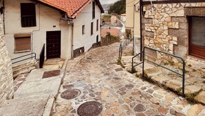 Eine schmale Kopfsteinpflasterstraße, gesäumt von Gebäuden mit Stein- und Stuckfassaden und einem Ziegeldach, unter einem wolkenlosen Himmel.