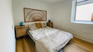 Ein Schlafzimmer mit einem Bett, Holznachttischen, einem Wandbild und einem Fenster.