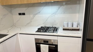A modern kitchen with white cabinets, a marble backsplash, a gas stove, an oven, and a stainless steel refrigerator.