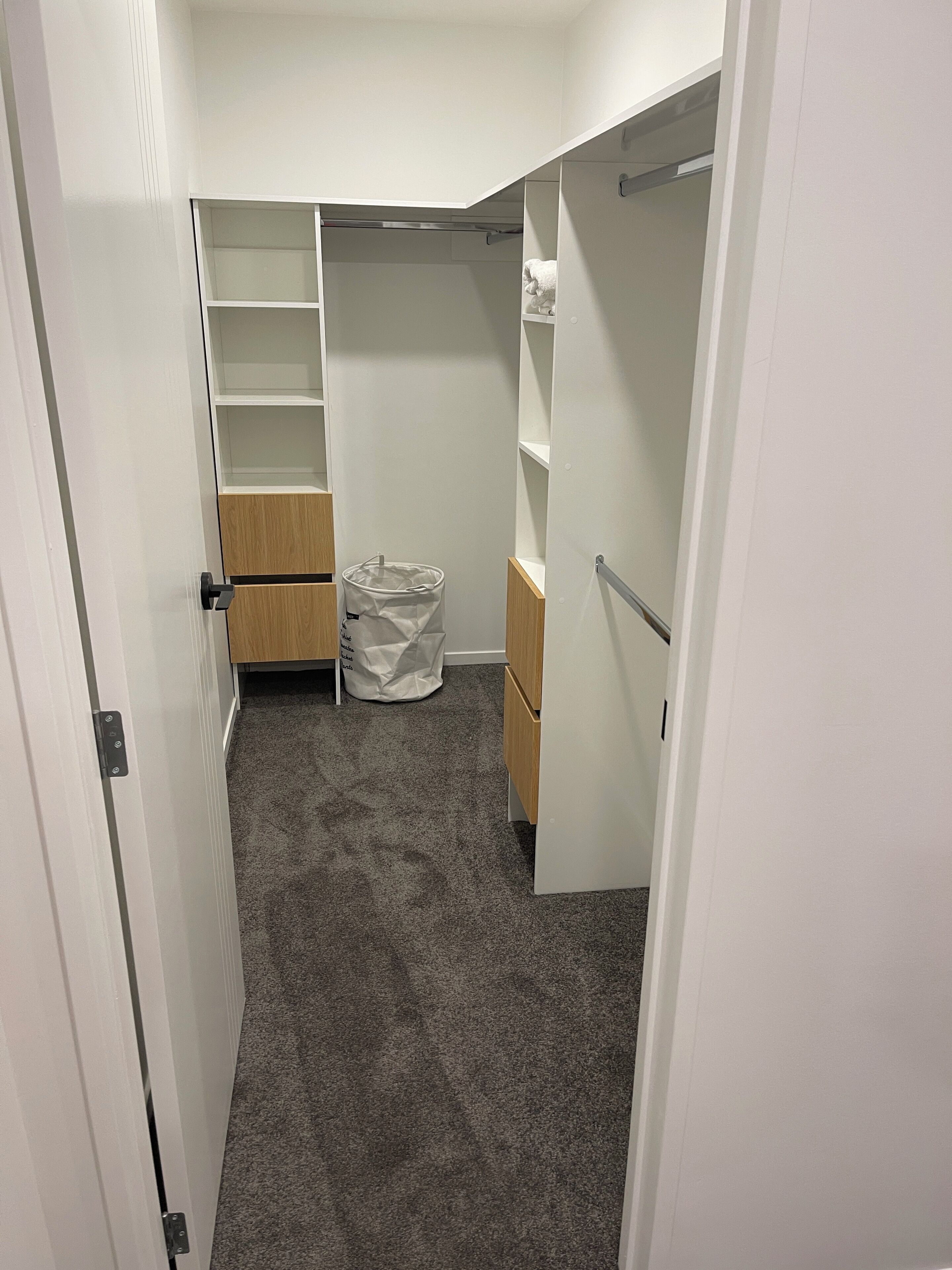 A walk-in closet with open shelves, a wooden cabinet, and a trash bag on the floor.