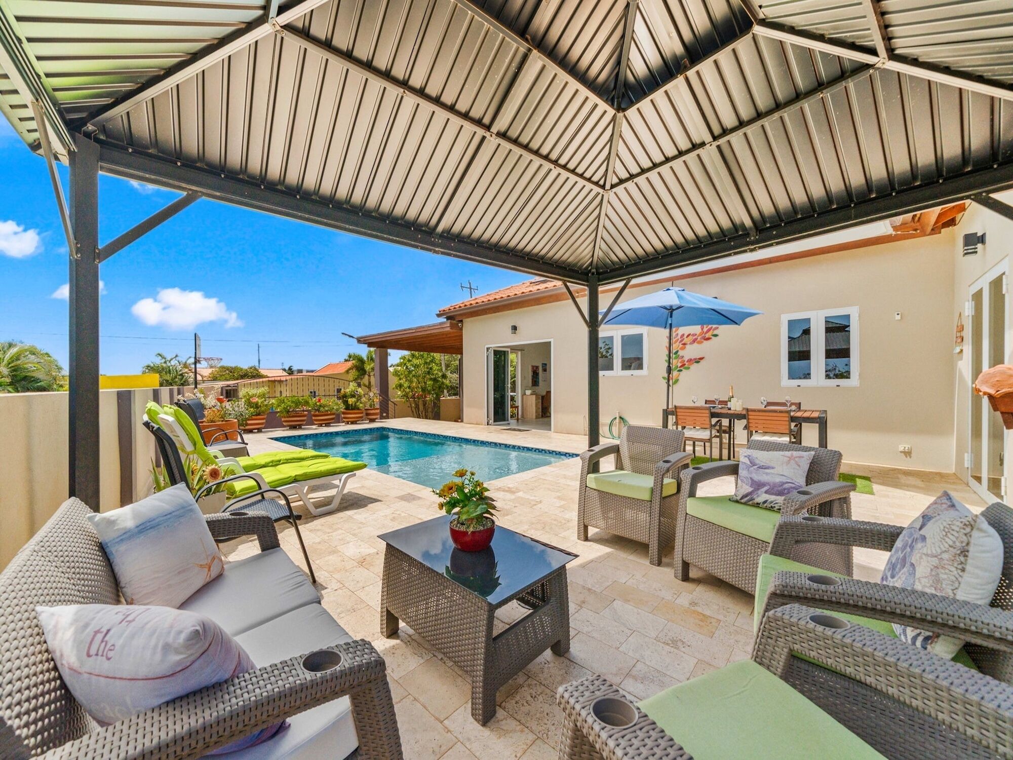 A covered outdoor area with a pool, lounge chairs, and a dining table.