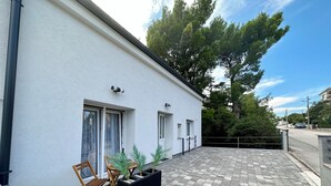 A modern building with a white exterior, large windows, and a paved patio area with outdoor furniture and planters. - Studio apartman Easy (Crikvenica)