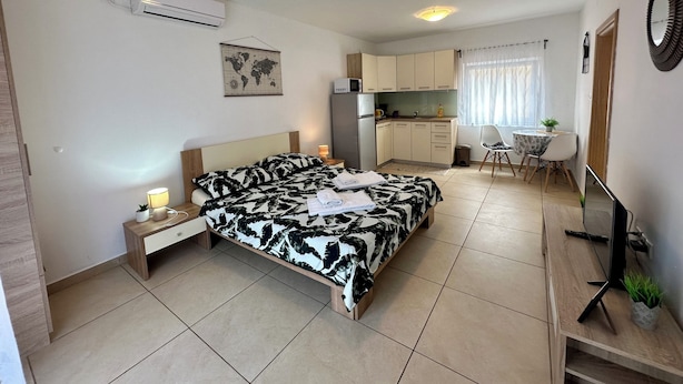 A compact hotel room with a bed, bedside table, lamp, and a kitchenette area. - Studio apartman Easy (Crikvenica)