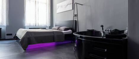 A modern bedroom with a bed, a vanity, and a large window.