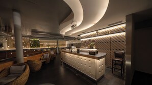 Un interior moderno con una zona de bar central, asientos acolchados y un diseño de techo único.