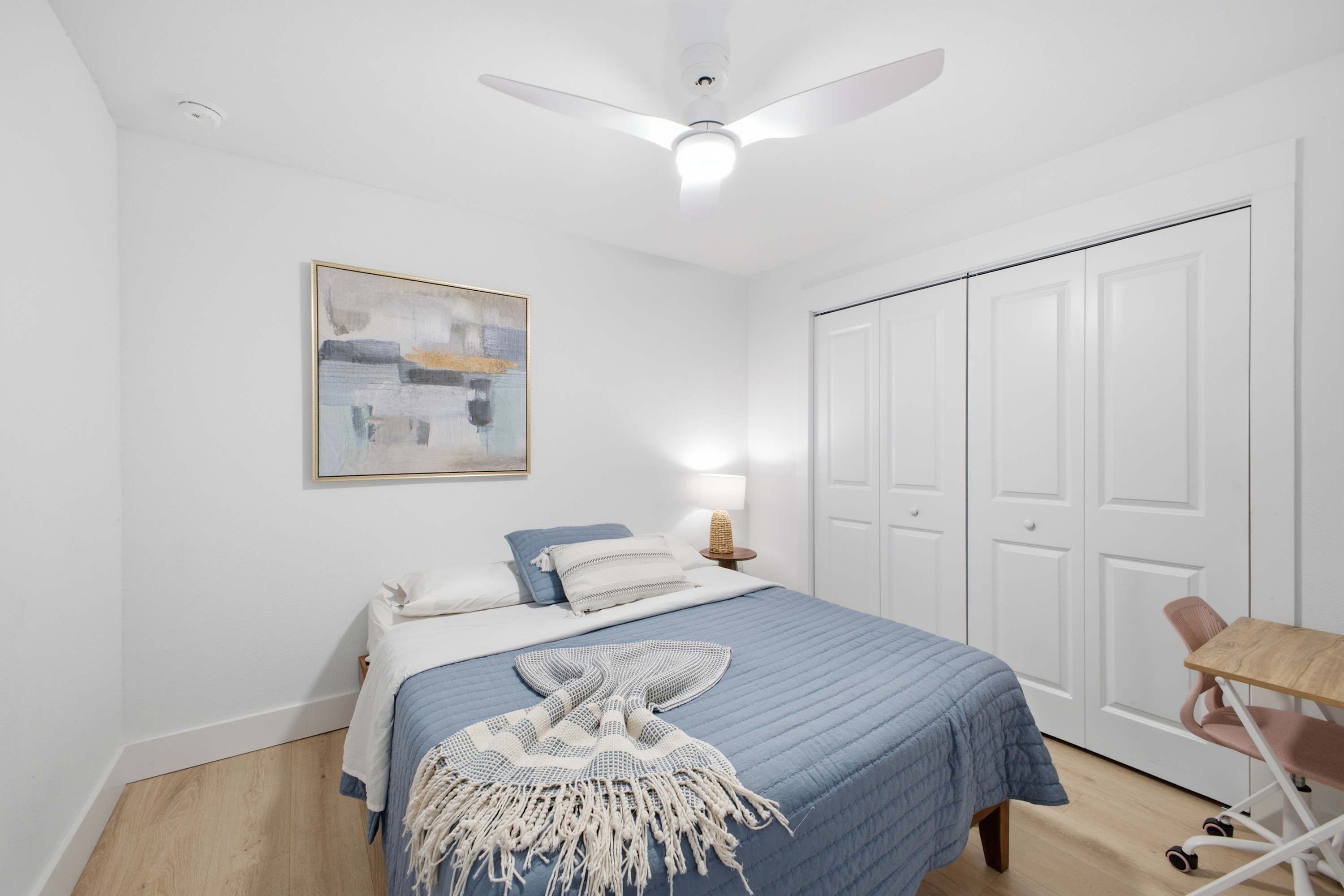 Une chambre à coucher comprenant un lit, un ventilateur de plafond, une lampe de chevet, une porte et une œuvre d’art accrochée au mur.