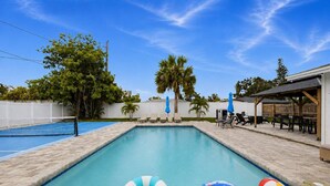 A swimming pool with lounge chairs and umbrellas, surrounded by palm trees and a covered patio area. - ‼️4BR Oasis w/ Heated Pool Near Anna Maria Island (Bradenton)