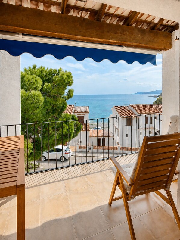 A balcony with a view of the sea and buildings, a white car parked outside, and a wooden chair. - Apartment with a terrace and ocean view - 3 bedrooms - Llançà (Cap de Creus) (Llançà)
