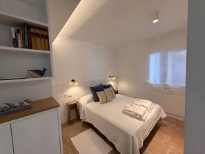 A bedroom with a bed, bedside tables, a shelf with books, a window, and a wall-mounted light fixture. - Apartment with a terrace and ocean view - 3 bedrooms - Llançà (Cap de Creus) (Llançà)