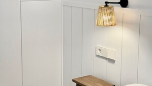 Et soveværelse med en seng, et sengebord, en vægmonteret lampe og en reol med bøger.