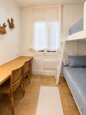 Ein Zimmer mit einem Etagenbett, einem Holztisch mit zwei Stühlen, einem Fenster mit Vorhängen und einem Fliesenboden.