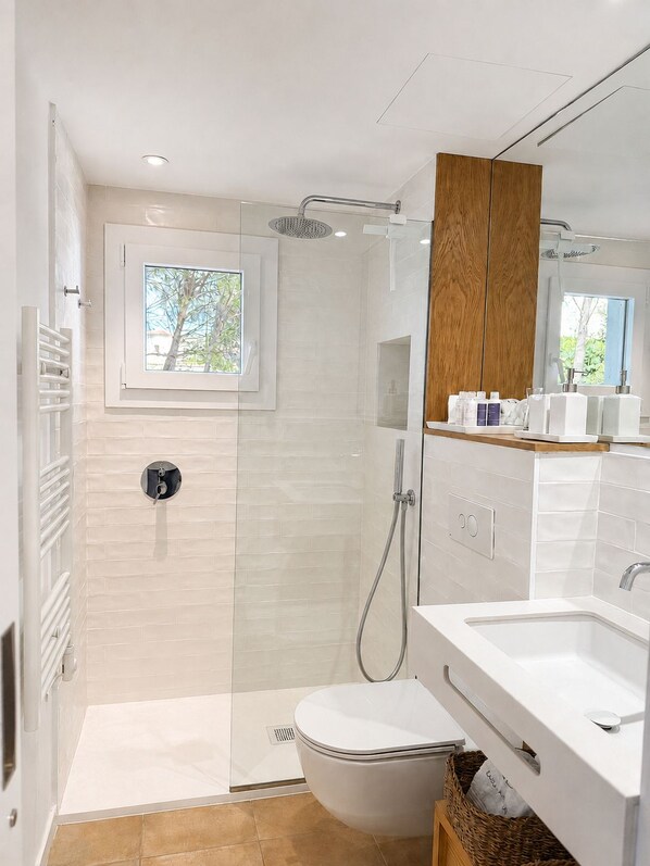 Ein modernes Badezimmer mit einer Glaskabine zur Dusche, einem weißen Waschbecken und einem Holzschrank über dem Spiegel.