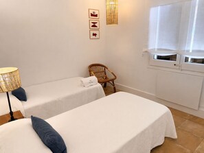 A hotel room with two beds, a wicker chair, a lamp, and a window with a view. - Apartment with terrace and sea view - 3 bedrooms - Llançà (Cap de Creus) (Llançà)