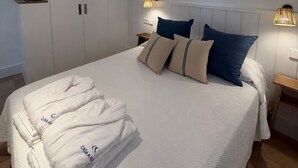 A neatly made bed with pillows and a folded robe, a wardrobe with shelves, and bedside lamps. - Apartment with terrace and sea view - 3 bedrooms - Llançà (Cap de Creus) (Llançà)