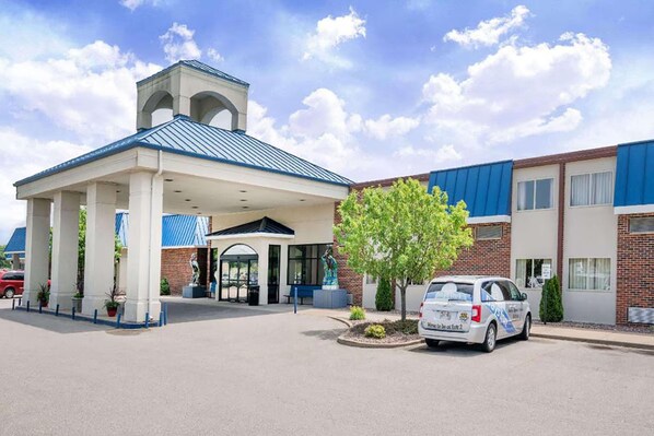 Un hotel con acceso cubierto, zona de estacionamiento y una estatua en su fachada.