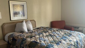 Una habitació d'hotel amb un llit, un quadre a la paret i una cadira vermella.