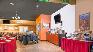 Zona de petit esmorzar amb taules, cadires, sistema de menjar a granel i un televisor a la paret.