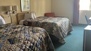 Habitació d'hotel amb dos llits, una taula, una cadira, una làmpada i una finestra amb cortines.