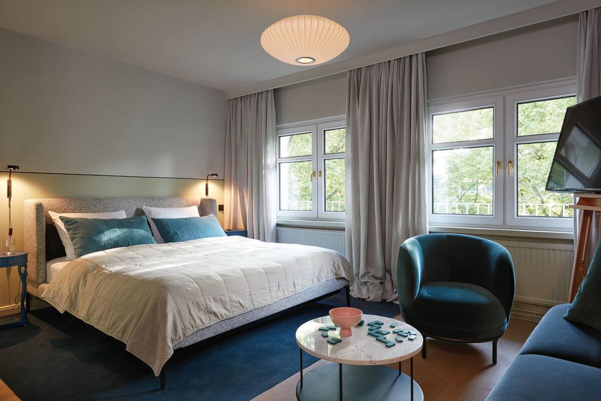 A bedroom with a bed, a chair, a table, and a TV.