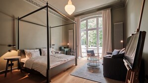 Un lit à baldaquin avec une table de chevet et une lampe, un canapé, une télévision et une grande fenêtre avec des rideaux.