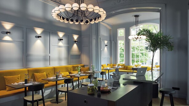 Un espace repas moderne avec un îlot central, des sièges jaunes et des luminaires suspendus.