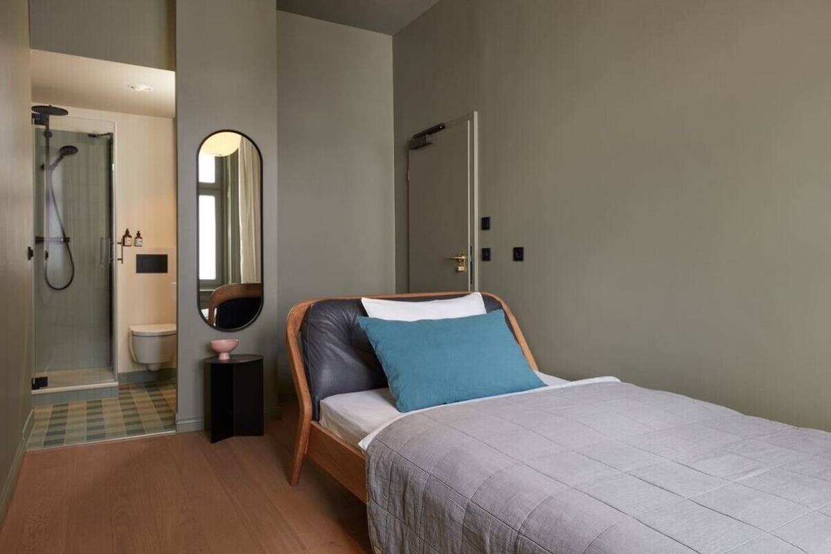 A bedroom with a bed, a mirror, a door, and a shower area.