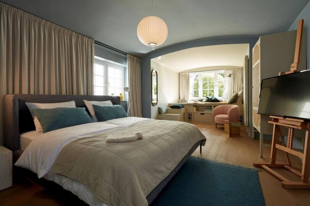 A modern bedroom with a large bed, a desk, a chair, and a television.