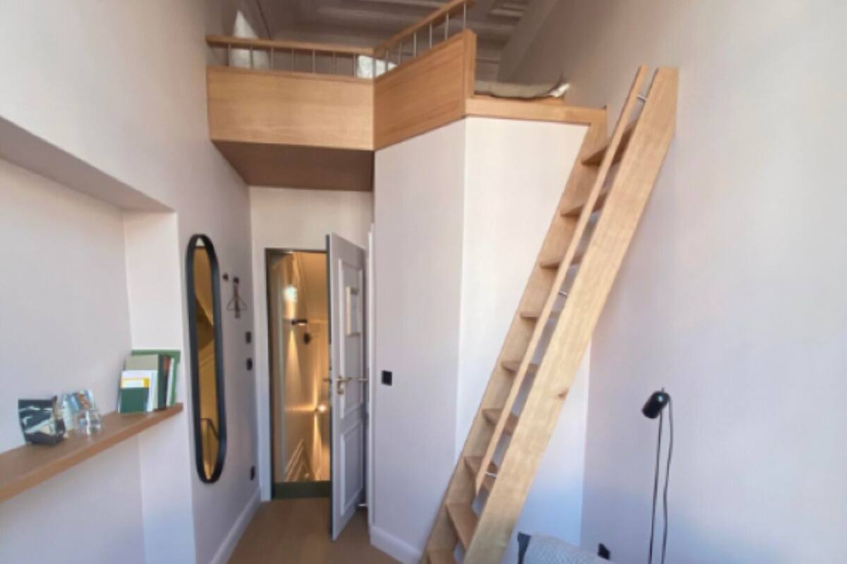 A modern interior with a loft bedroom, wooden staircase, and a blue sofa.