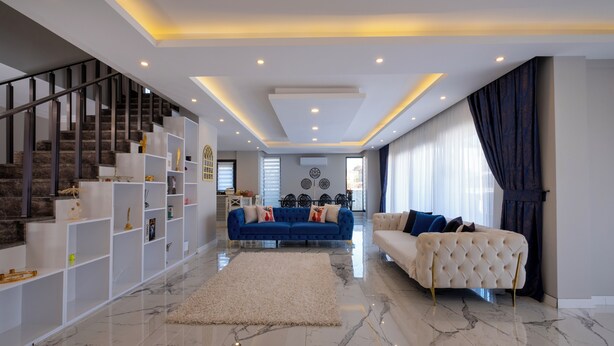 A spacious living area with a marble floor, a blue sofa, a white sofa, a staircase with a glass railing, and a dining area in the background. - Luxury Private Pool Villa in Fethiye6En-Suite Bedrooms Sleeps12  Sea&Nature View (Mugla)