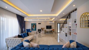 A modern living room with a large blue sofa, a white tufted sofa, and a TV on the wall. - Luxury Private Pool Villa in Fethiye6En-Suite Bedrooms Sleeps12  Sea&Nature View (Mugla)