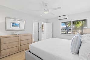 A bedroom with a bed, a ceiling fan, a window with a view, a dresser, and a framed picture on the wall.