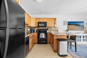 A modern kitchen with wooden cabinets, a black refrigerator, a microwave, and a granite countertop.
