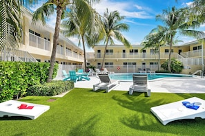 A pool area with lounge chairs and a swimming pool surrounded by palm trees and a building with balconies.