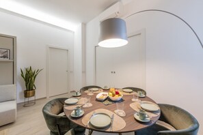 Een eetgedeelte met een ronde tafel voor vier personen, omringd door stoelen, een potplant en een moderne hanglamp.